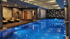 A modern indoor swimming pool with a blue mosaic floor, lounge chairs, and a geometric wall design. - Sofitel Istanbul Taksim (Istanbul)