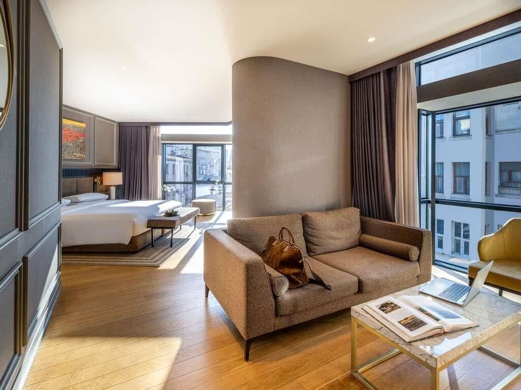 A modern hotel room with a bed, a sofa, a coffee table, and a view of the city.