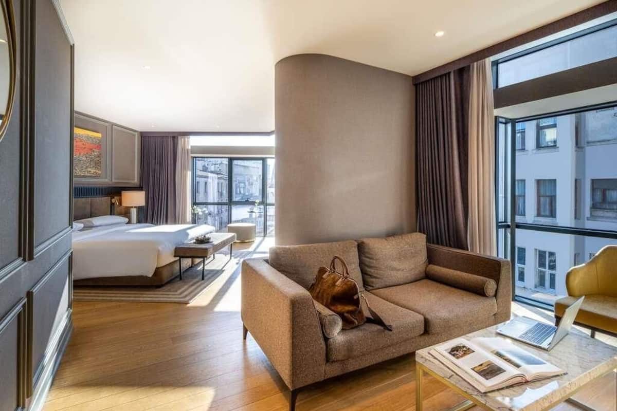 A modern hotel room with a bed, a sofa, a coffee table, and a view of the city.