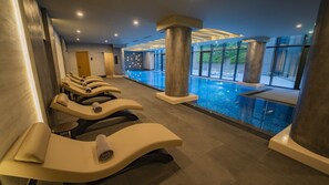 Un espace spa moderne doté de fauteuils inclinables, d’une grande piscine intérieure et de larges fenêtres offrant une vue sur l’extérieur.