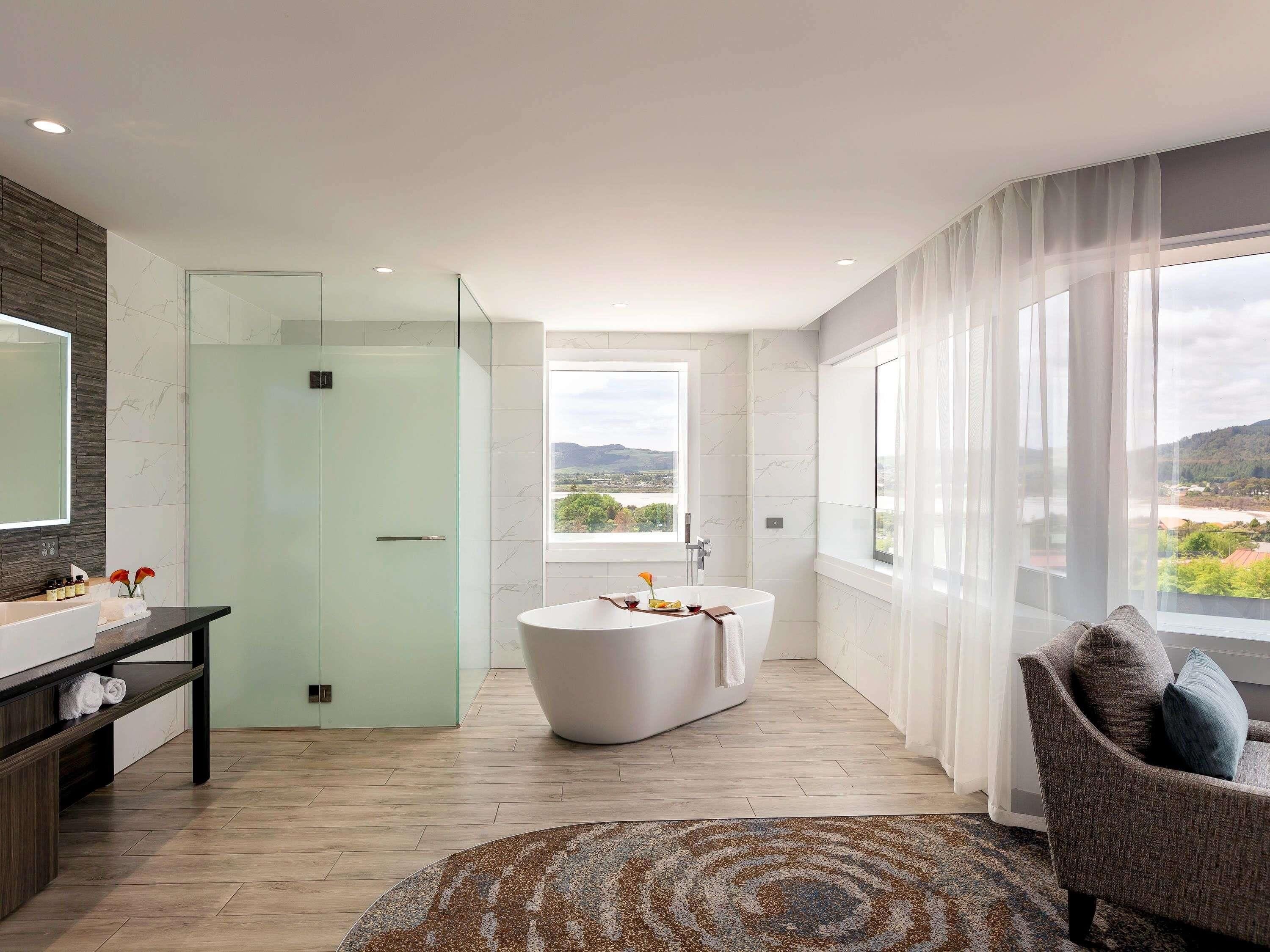 A modern bathroom with a bathtub, a glass shower enclosure, and a large window offering a view.