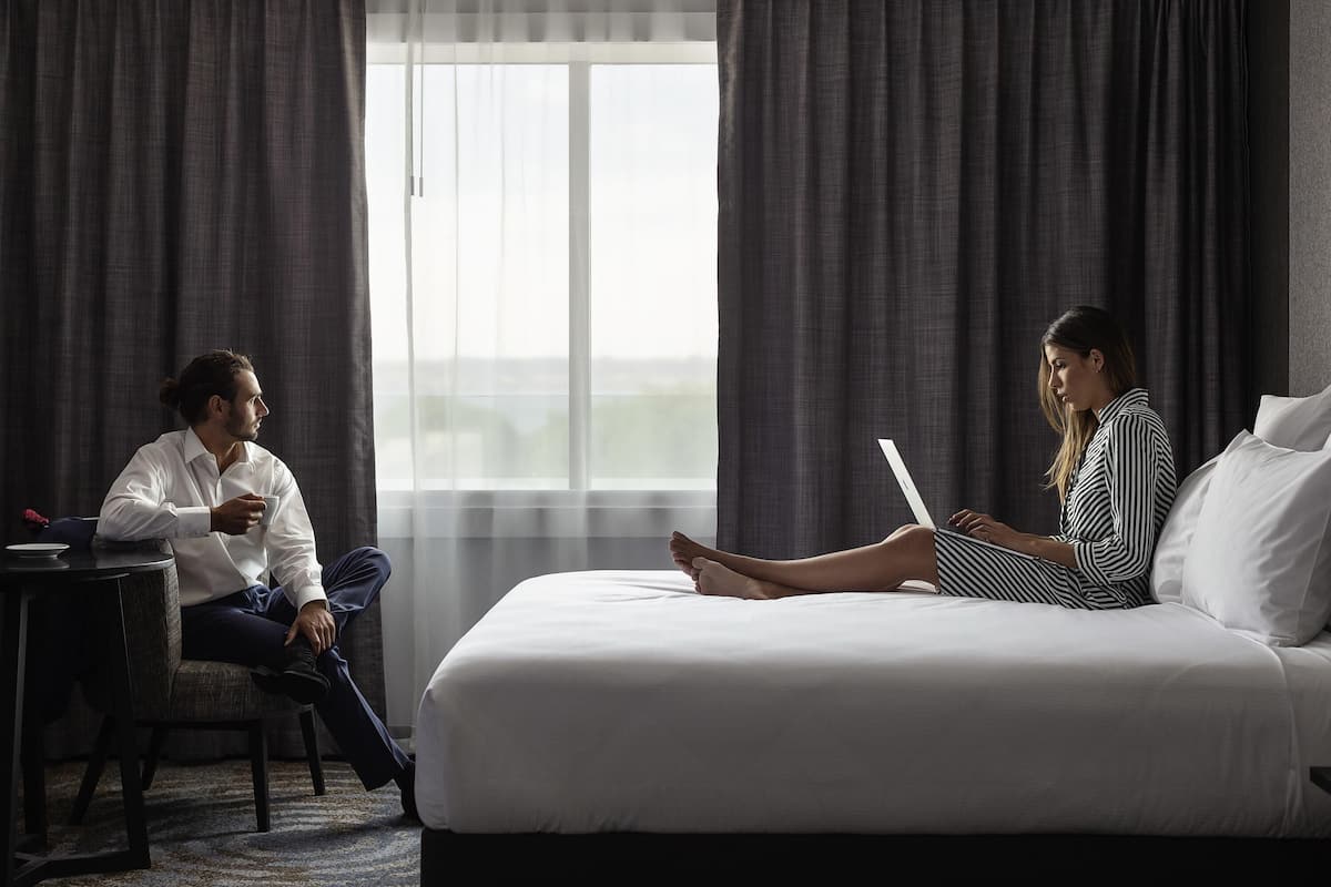 Una habitación de hotel con una cama grande, una mesita pequeña y un ventanal con cortinas.
