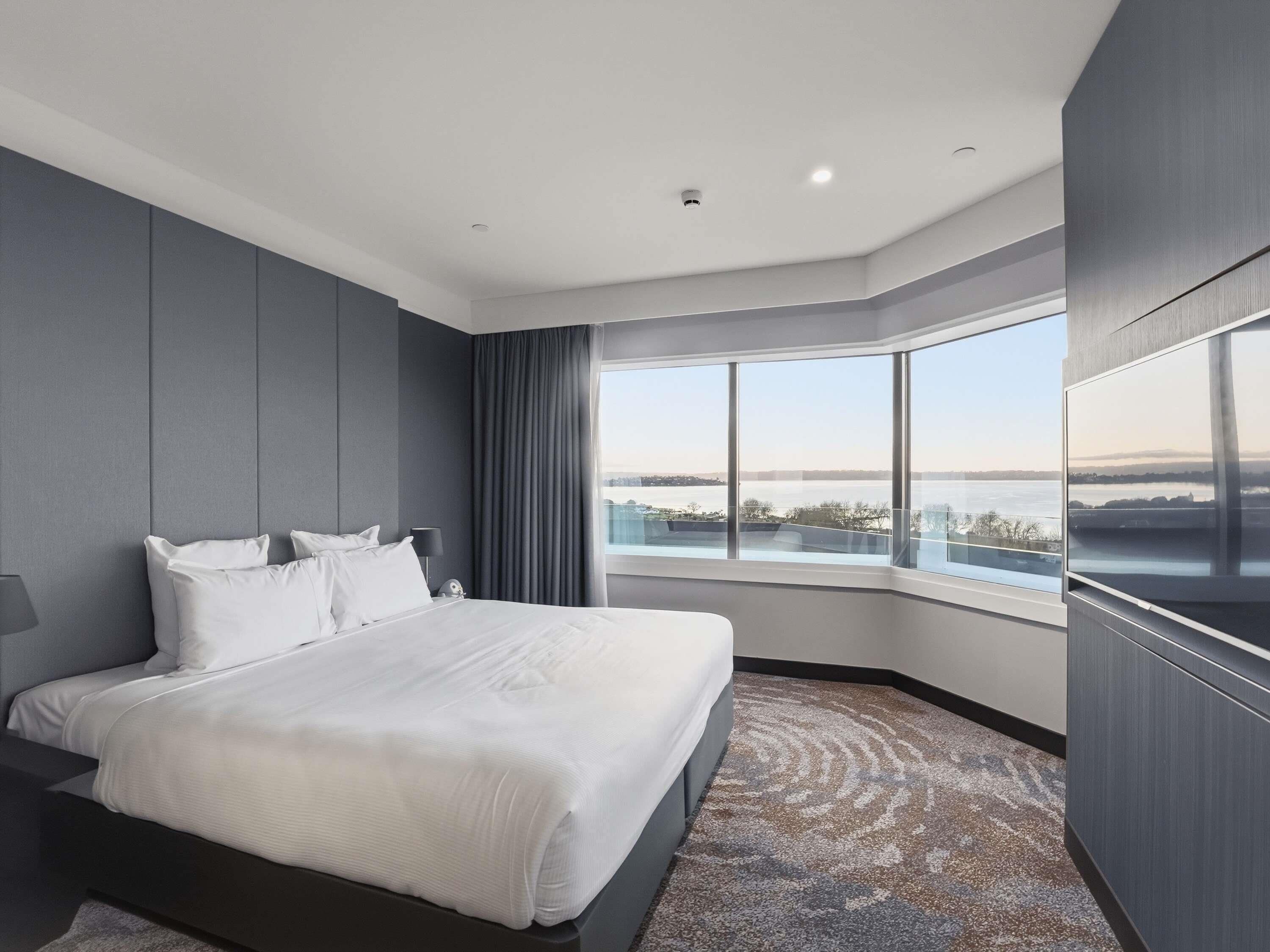 A modern hotel room with a large bed, a TV, and a view of a body of water.