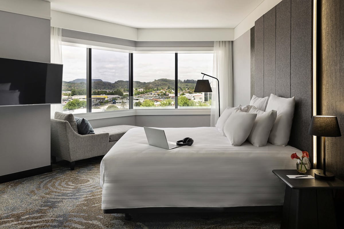 Una habitación de hotel moderna con una cama grande, un sofá, un televisor y vistas a un paisaje urbano.