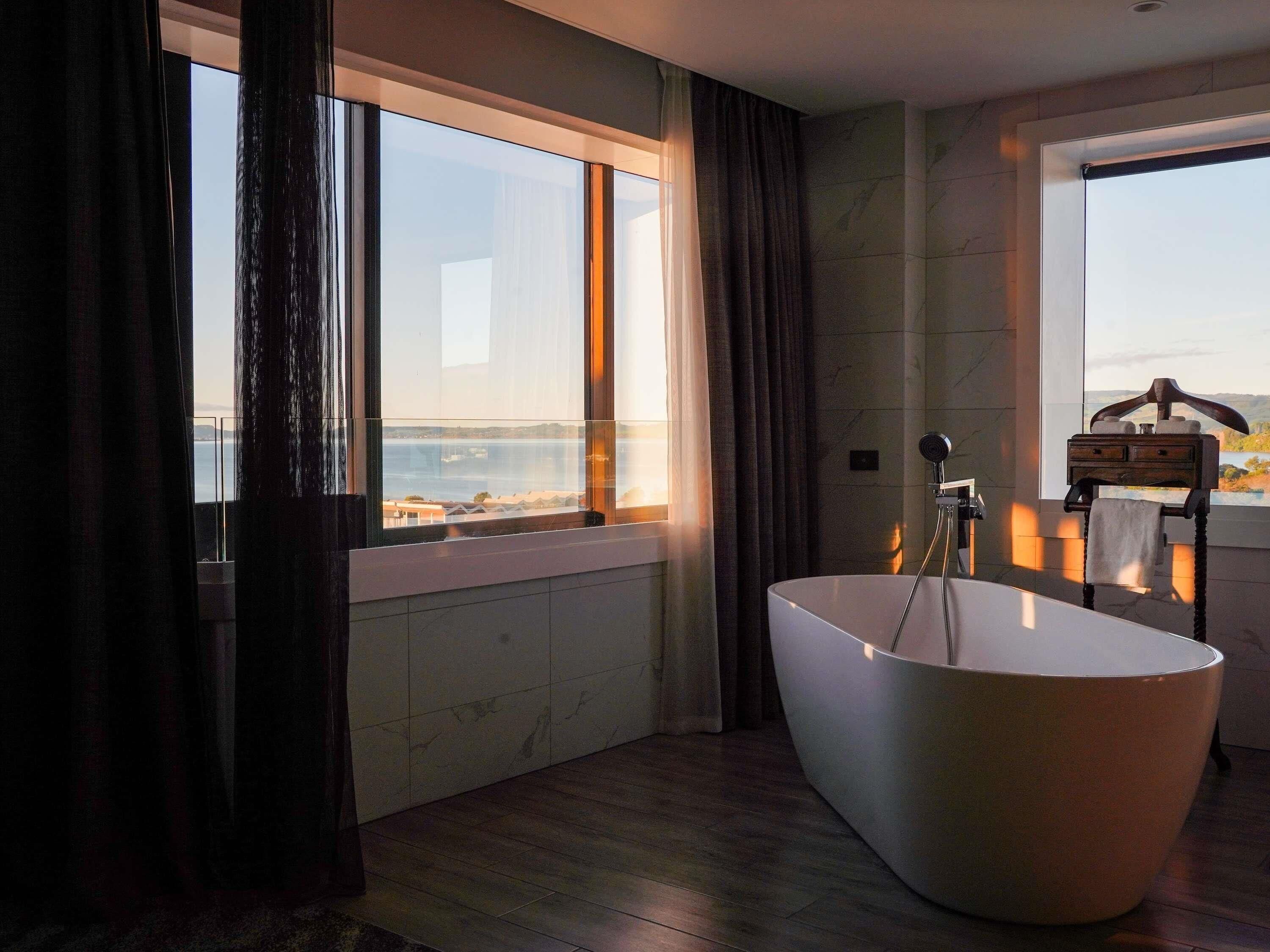 Une salle de bain moderne avec une baignoire sur pieds, une fenêtre donnant sur la mer et un porte-serviettes en bois.