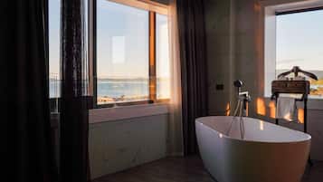 Une salle de bain moderne avec une baignoire sur pieds, une fenêtre donnant sur la mer et un porte-serviettes en bois.