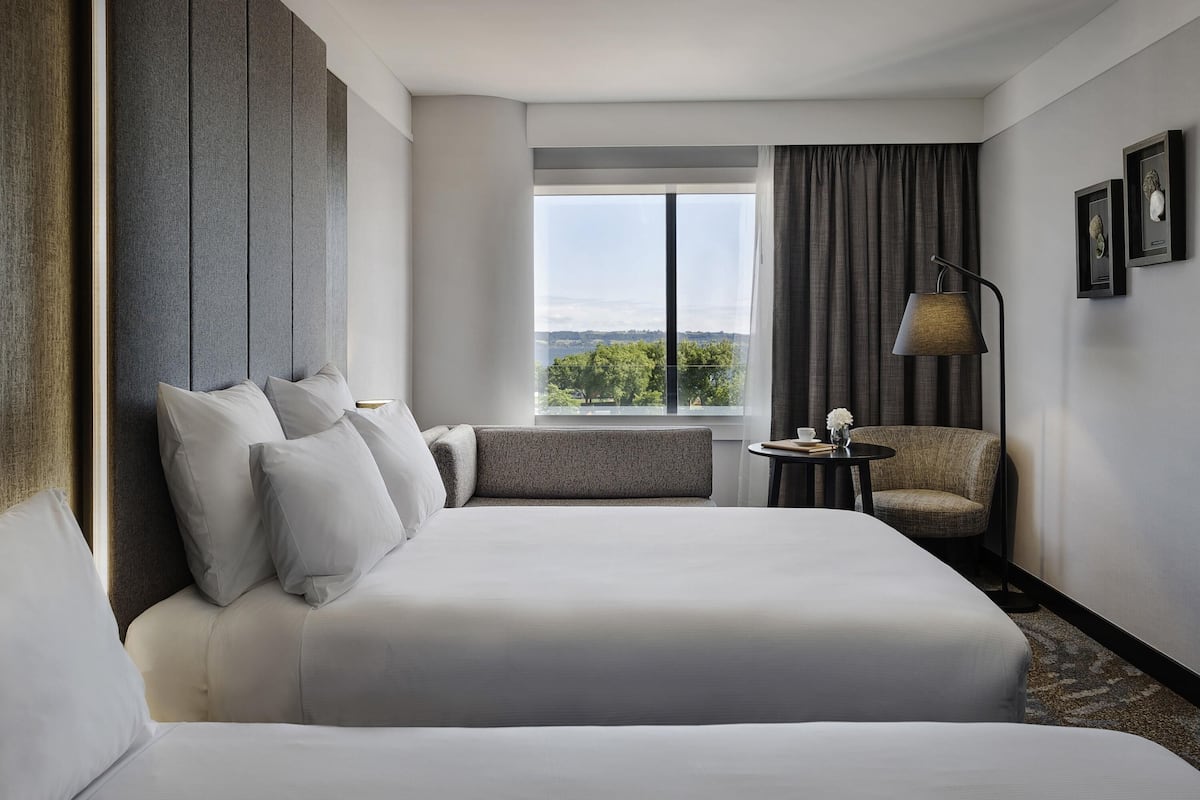 A hotel room with a large bed, a sofa, a small table, a lamp, and a window with a view.