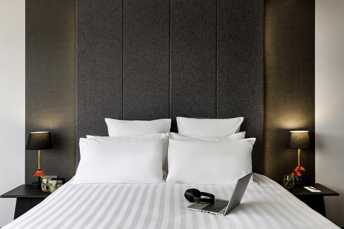 A hotel room with a large bed, two bedside tables, a laptop, and a vase with flowers.