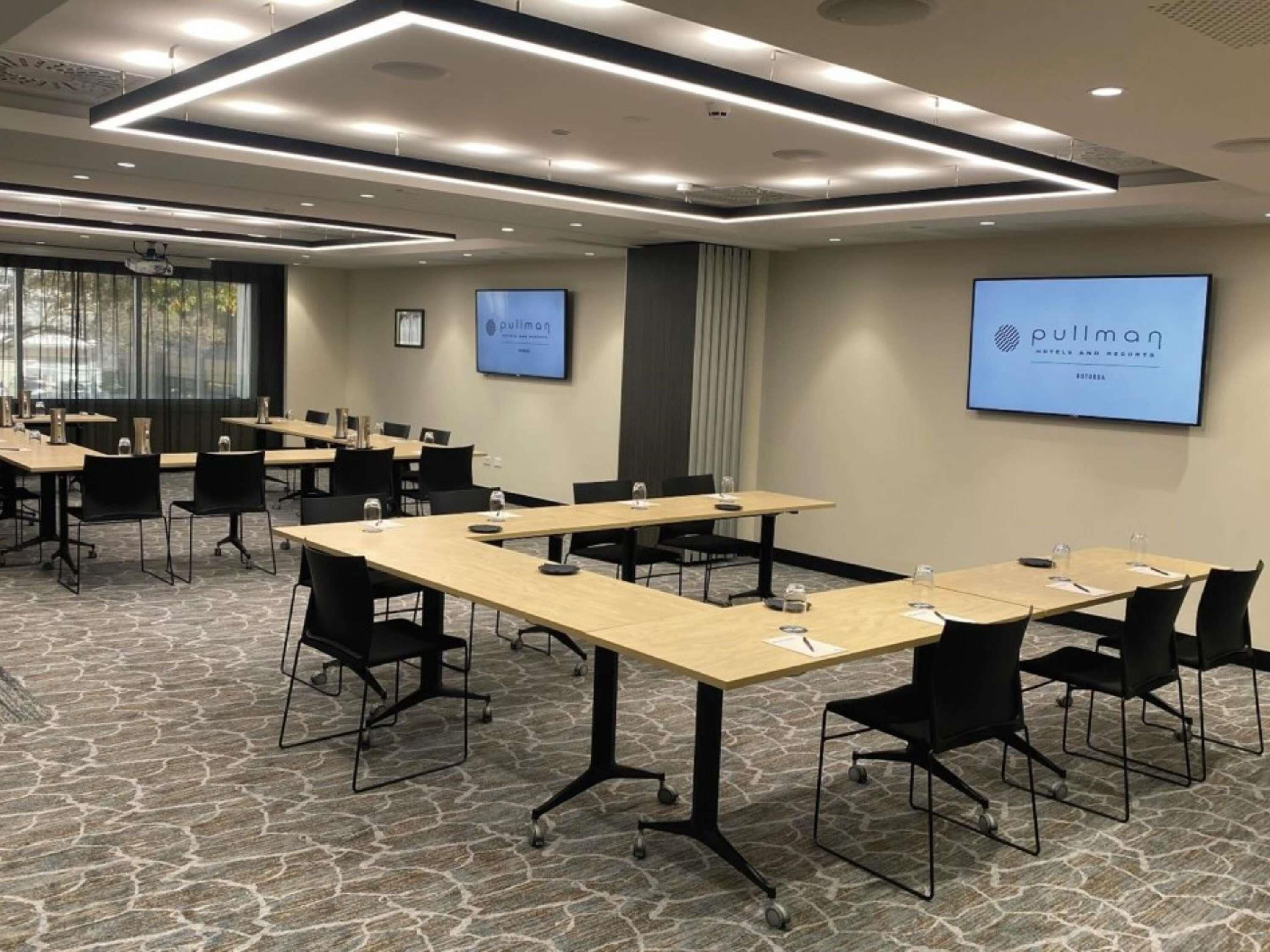 Ein Konferenzraum mit Tischen, Stühlen und einer großen Leinwand, auf der der Name des Hotels zu sehen ist.