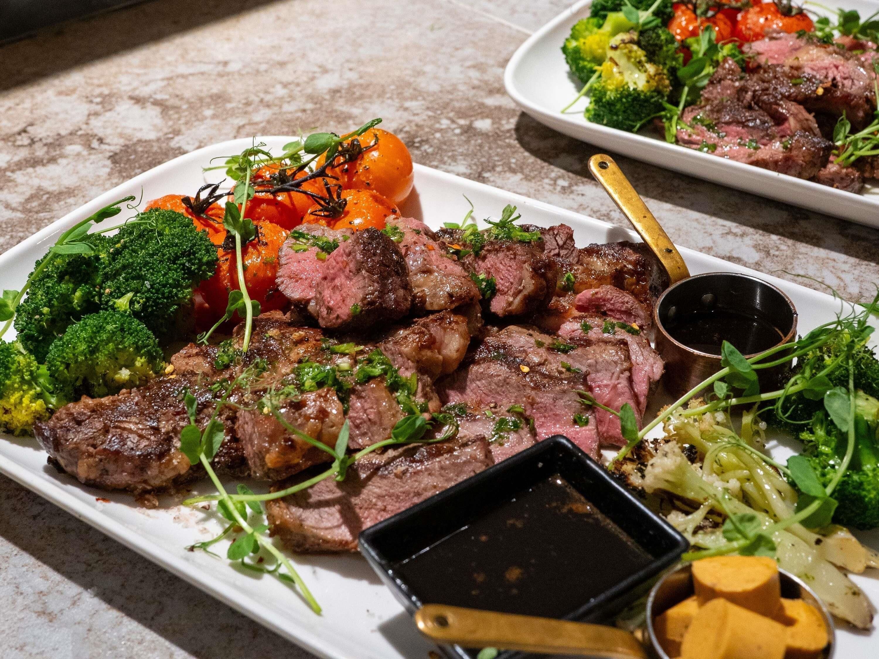 A plate of steak with vegetables and a sauce container.