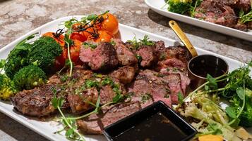 A plate of steak with vegetables and a sauce container.