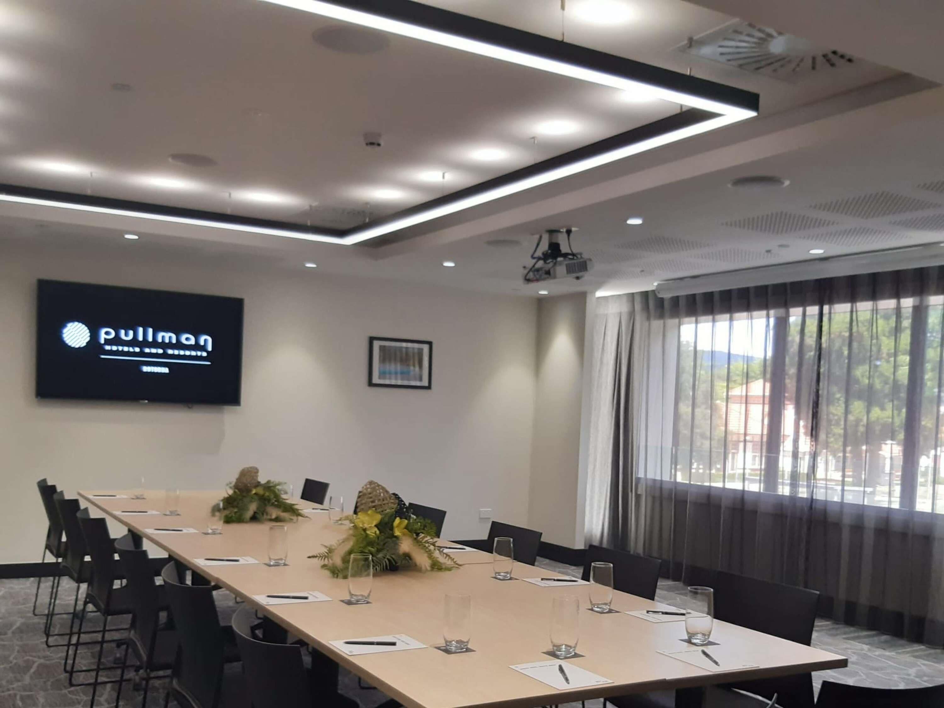 Un salón de conferencias con una larga mesa, sillas, una pantalla de televisión y un proyector.