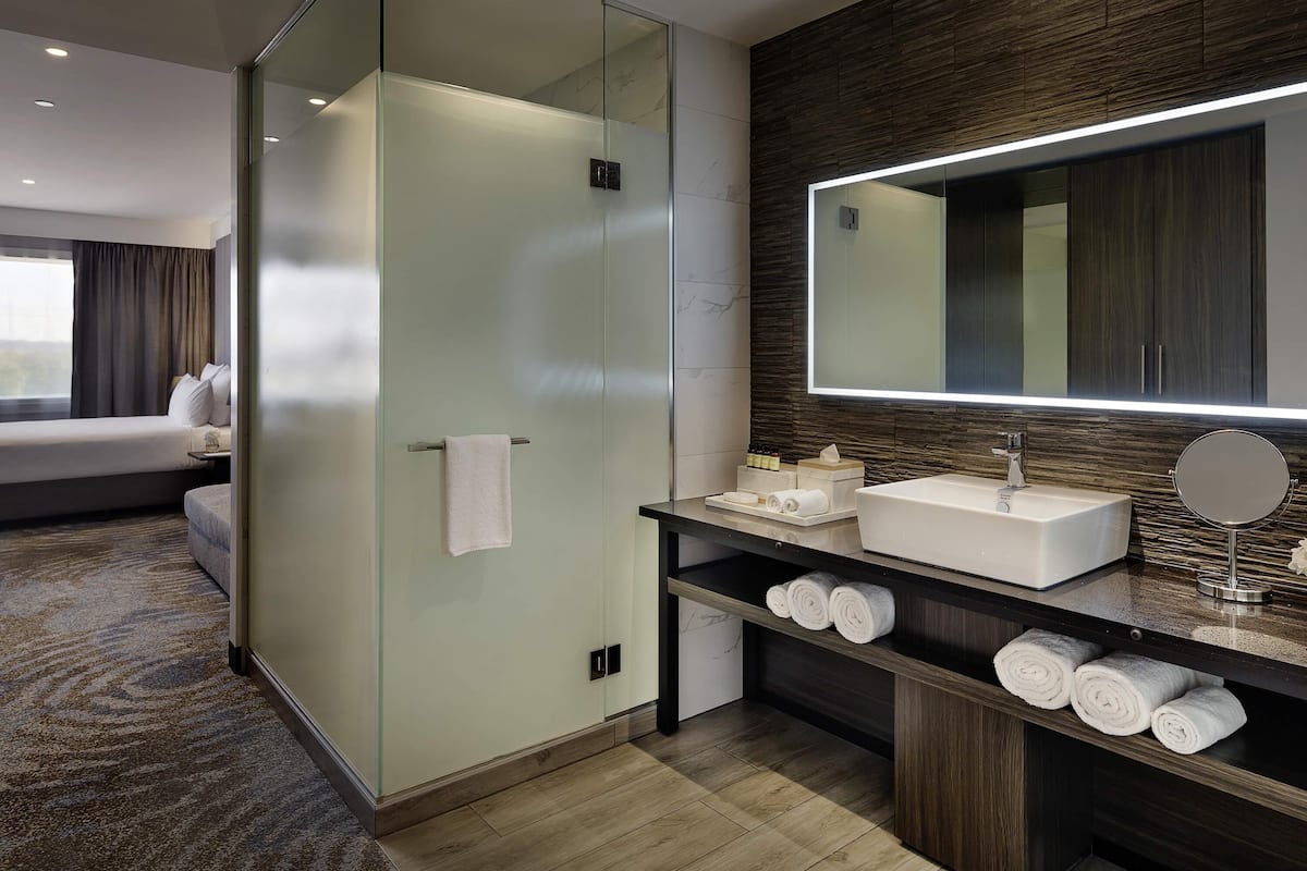 A modern bathroom with a glass-enclosed shower, a vanity with a large mirror, and neatly rolled towels.