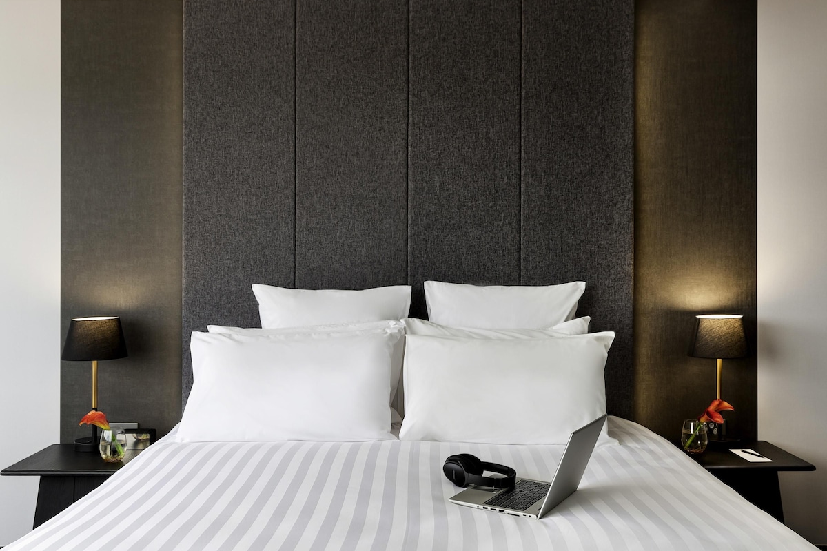 A hotel room with a large bed, two bedside tables, a laptop, and a vase with flowers.