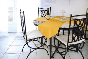 A dining area with a round table, four chairs, a yellow tablecloth, a wine bottle, and a glass.