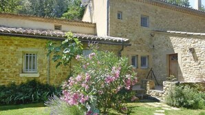 A stone building with a garden in front, featuring a small tree with pink flowers. - Apartment in Caderousse with Pool (Caderousse)