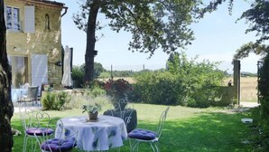 A stone building with a dining area featuring white metal chairs and a table with a white tablecloth. - Apartment in Caderousse with Pool (Caderousse)