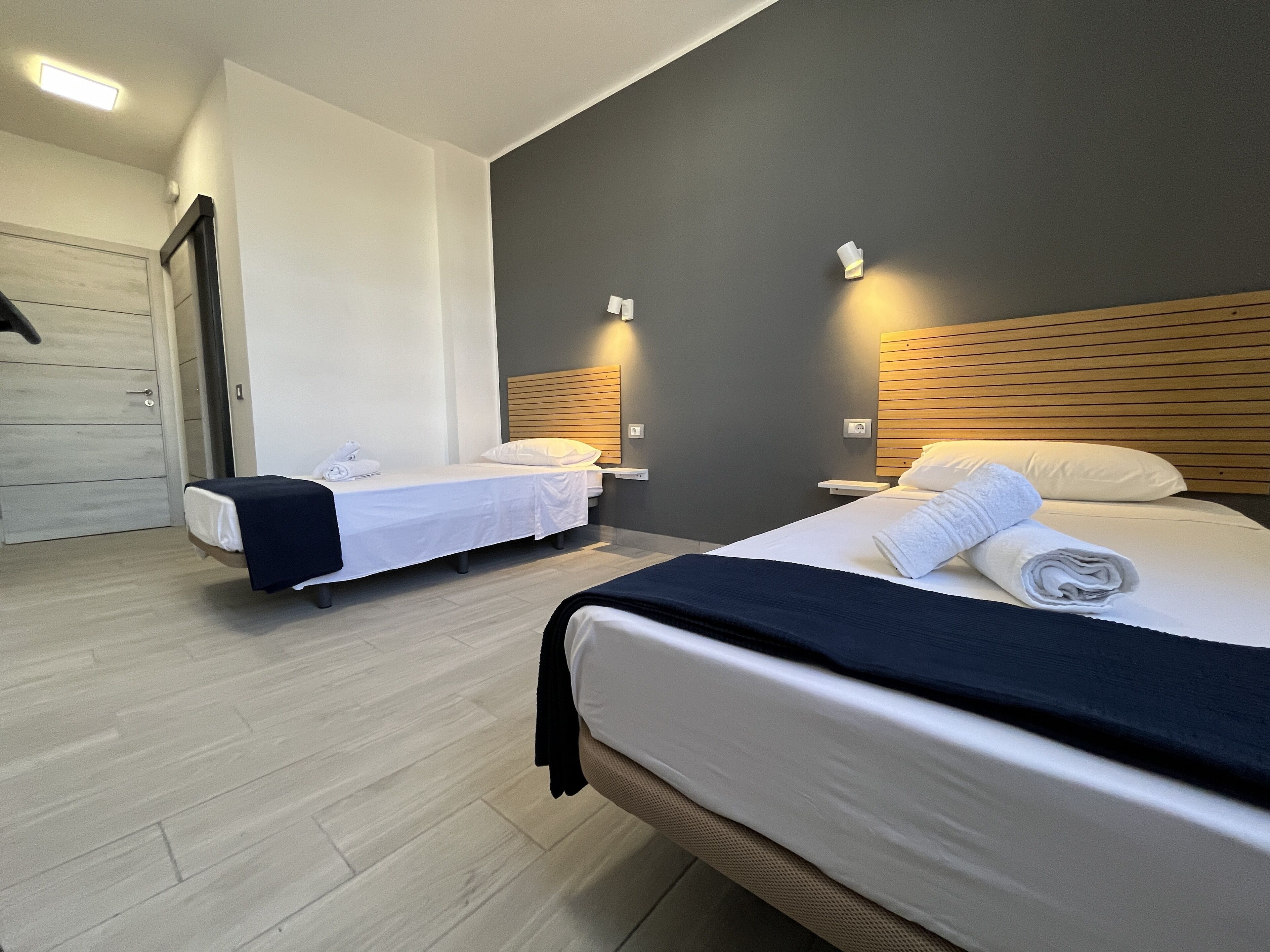 Habitación de hotel con dos camas, cabecero de madera, piso de color claro y puerta blanca.