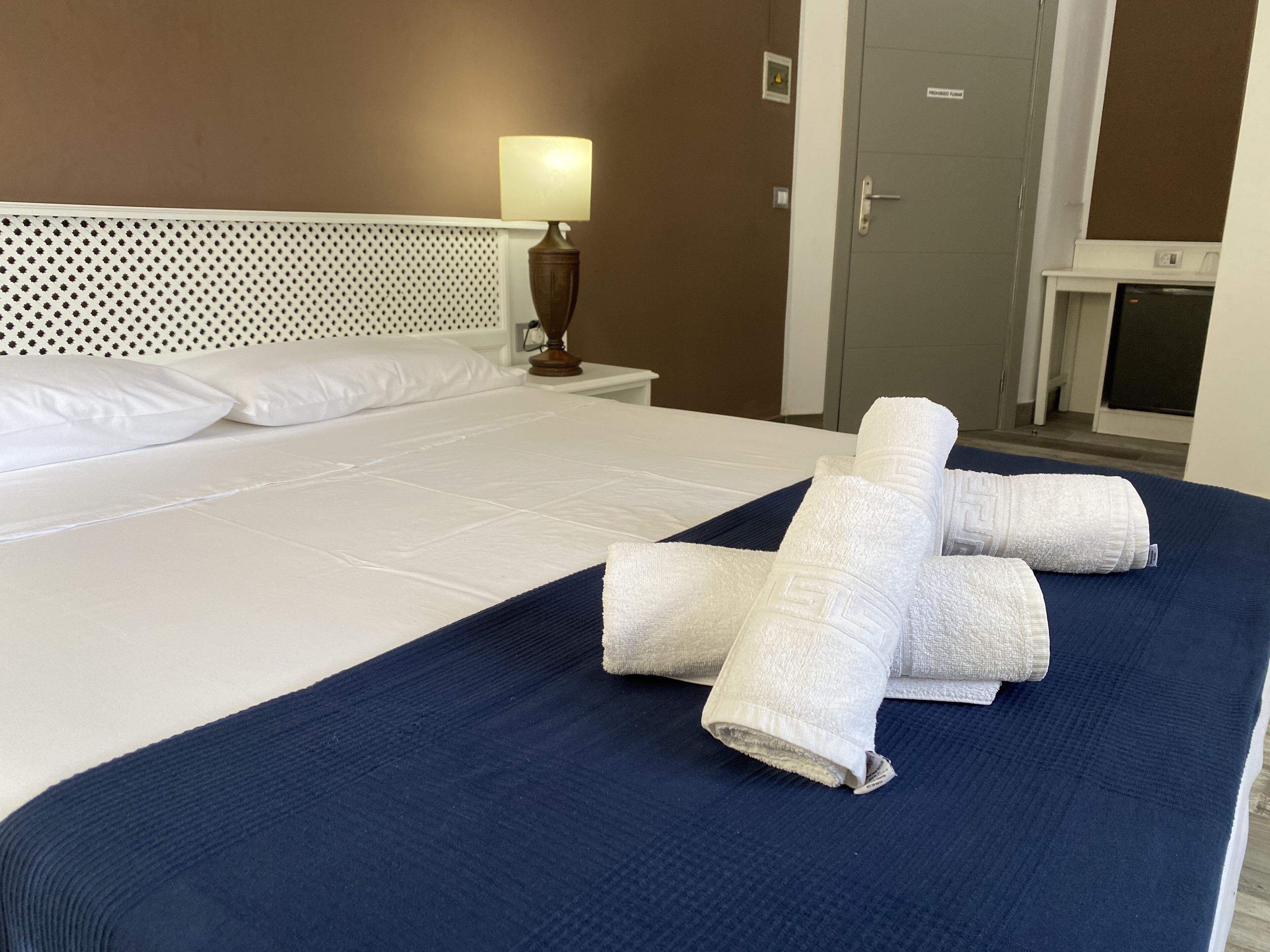 Ein ordentlich gemachtes Bett mit weißen Leinen, einer blauen Tagesdecke und gefalteten Handtüchern.