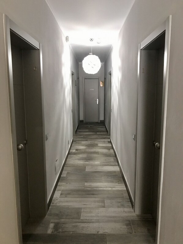 Un pasillo estrecho con suelo de madera, puertas a ambos lados y una lámpara en el centro.