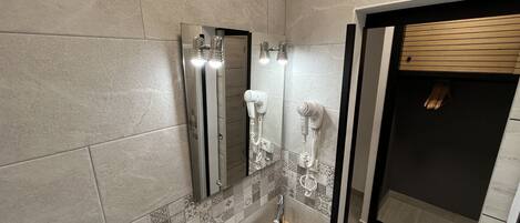 A modern bathroom with a large mirror, a sink, and two hair dryers mounted on the wall.