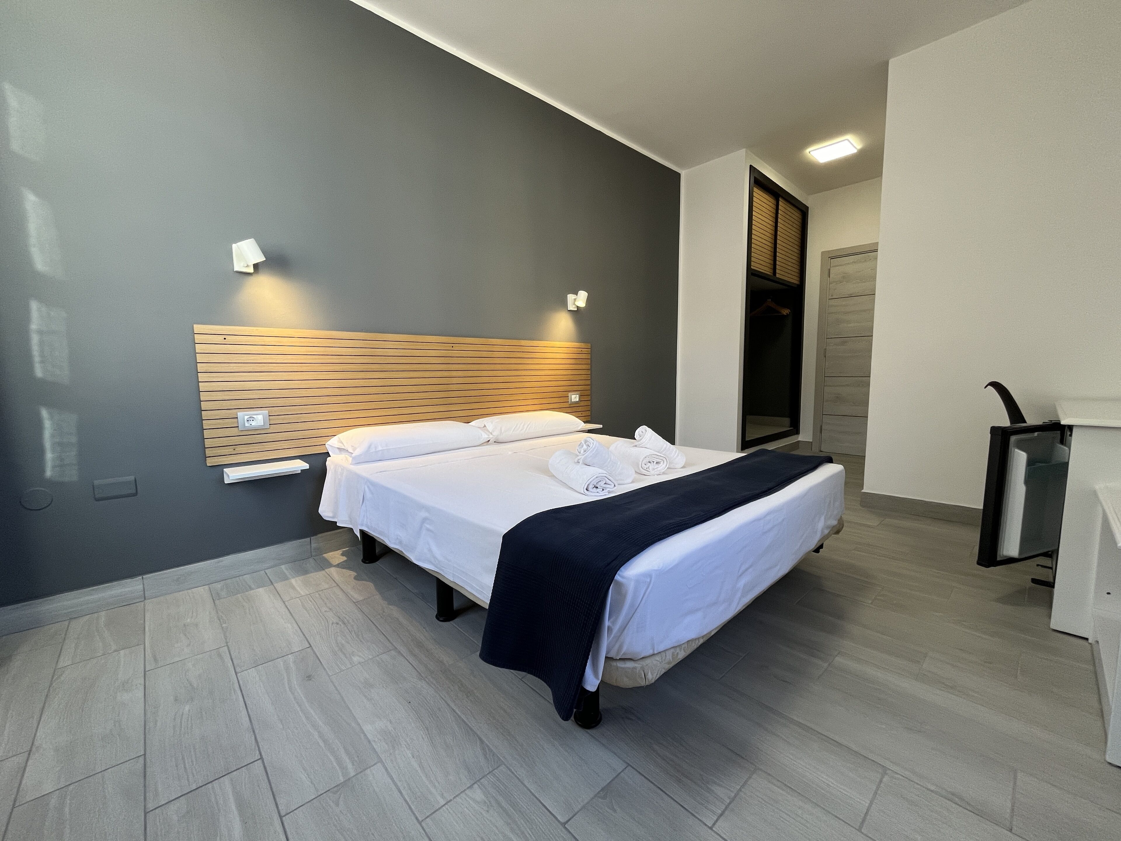 Ein modernes Hotelzimmer mit einem Bett, einem Holz-Kopfteil und einem integrierten Kleiderschrank.