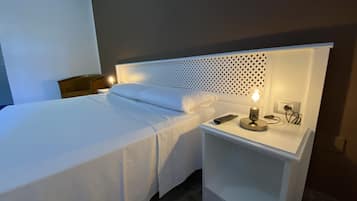 A neatly made bed with white linens, a bedside lamp, and a remote control on a white nightstand.