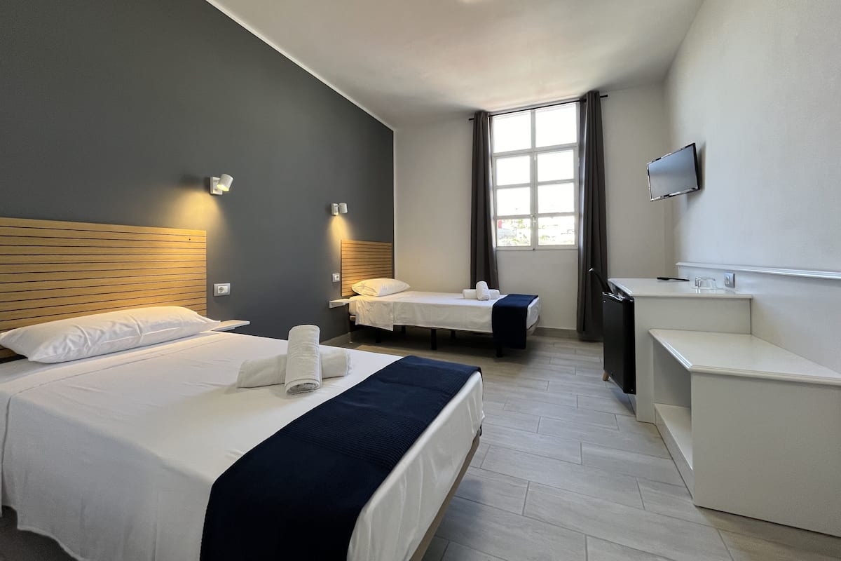 A hotel room with two beds, a desk, a TV, and a window with curtains.
