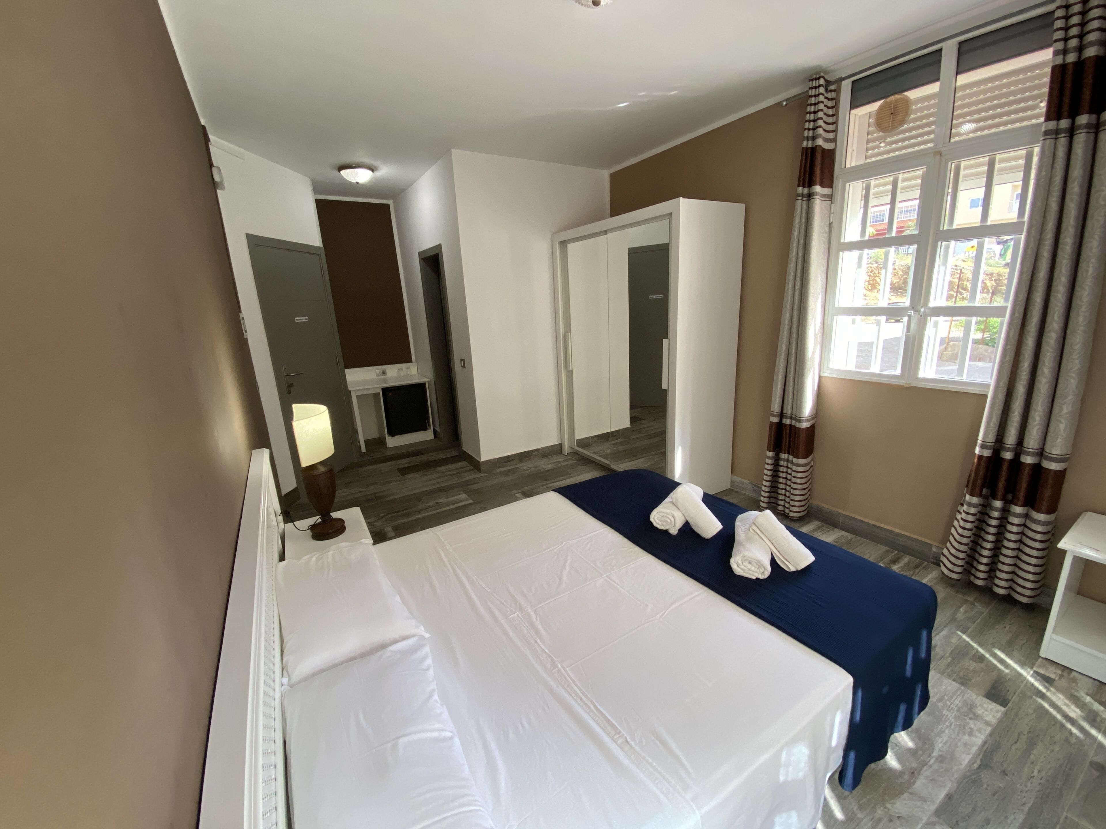 Une chambre d’hôtel avec un lit, un bureau, une lampe, une fenêtre avec des rideaux et une vue sur l’extérieur.