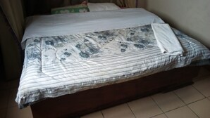 Una cama con colcha estampada, un cojín blanco y una cortina color beige.