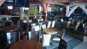 Un restaurante con mesas y sillas redondas, una zona de bar y un techo estampado.