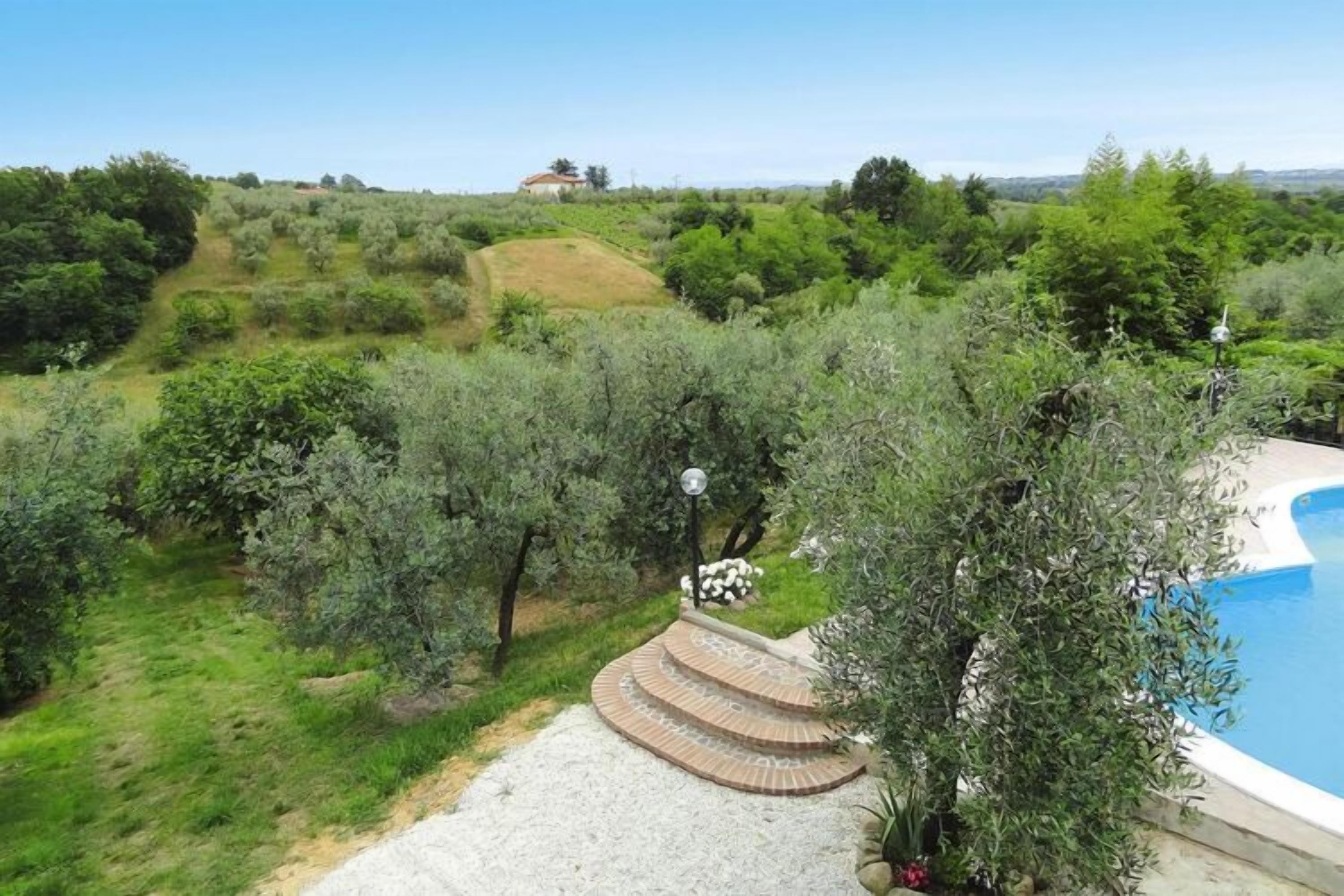 Un espace piscine avec un chemin de pierre menant à une maison, le tout situé dans un paysage luxuriant et verdoyant.