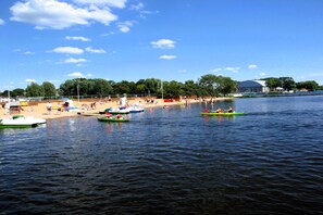 Un lago con barcos, una playa arenosa y árboles al fondo.
