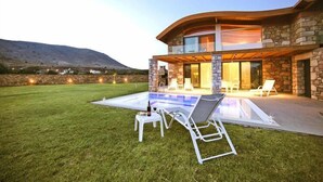 Una casa moderna con piscina, fachada de piedra y mobiliario de exterior.