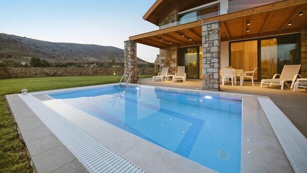 Una casa moderna con piscina, pilares de piedra y un patio con sillones de descanso.