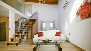 Amplia sala de estar con escalera, un sofá blanco con cojines rojos y una mesa de centro de vidrio.