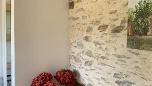 Eine Ecke eines Raumes mit einer Steinsäule, einem kleinen Holzschrank und einer Vase mit roten Blumen.