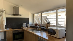 Eine moderne Küche mit Holzausstattung, Edelstahlgeräten, einem Backofen, einem Geschirrspüler und einem Fenster mit Blick auf eine Holzterrasse und Treppe.