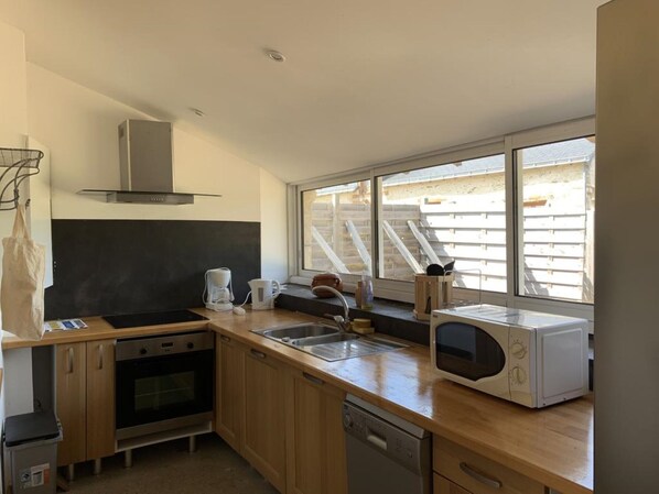 Una cocina moderna con armarios de madera, electrodomésticos de acero inoxidable y un ventanal con vistas a un edificio con escaleras.