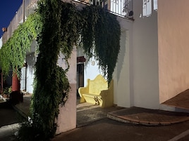Un edificio con un banco amarillo debajo de un arco cubierto de hiedra.