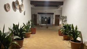 A hallway with potted plants on either side, leading to a room with a wooden ceiling and a door at the end. - Apartamentos Turísticos Los Alisos (Aliseda)