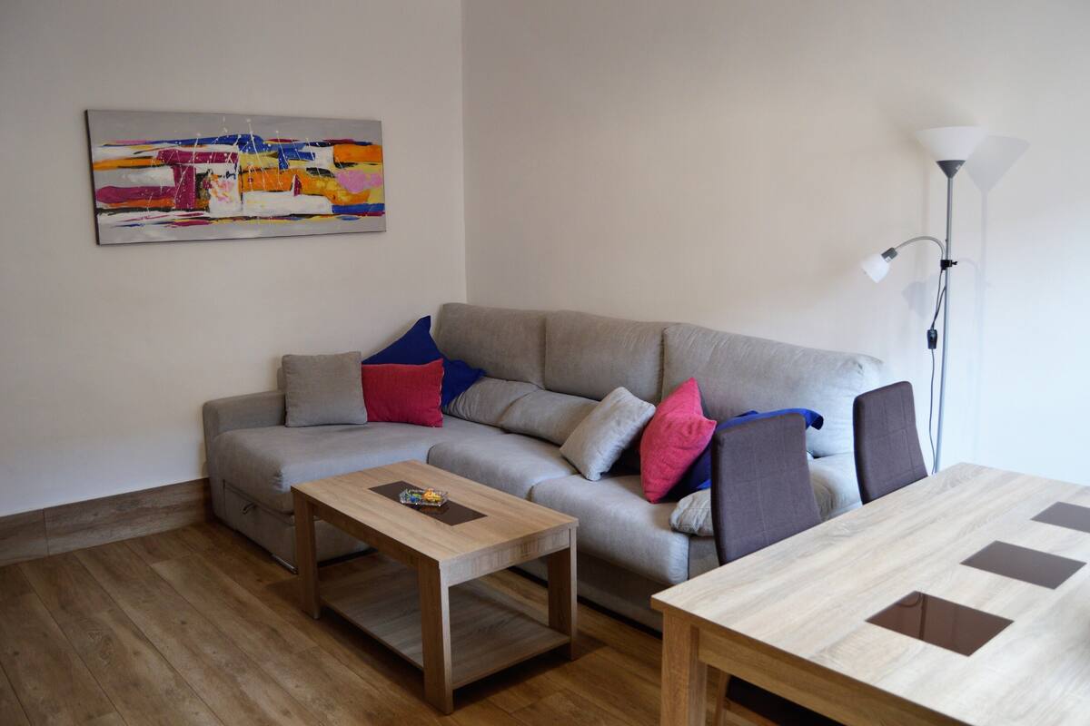 A living room with a grey sofa, two wooden tables, and a floor lamp.