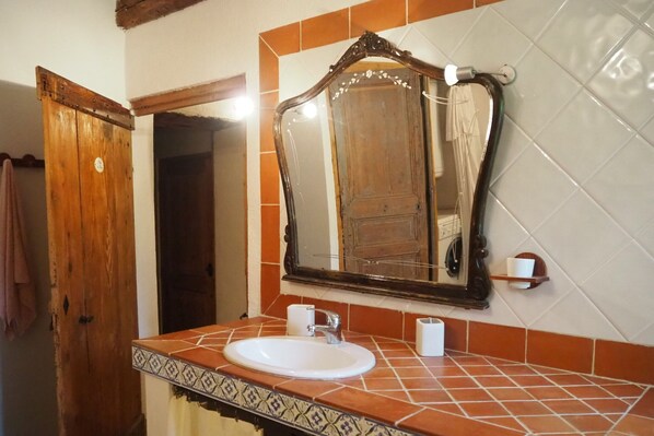 Une salle de bain avec un lavabo blanc, une porte en bois et un miroir doté d’un cadre décoratif.