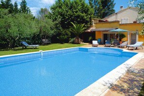 Una piscina con sillones de descanso y una casa al fondo.