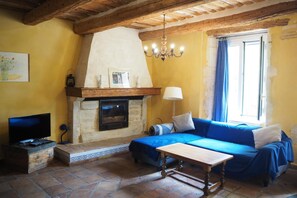 A cozy living room with a stone fireplace, a blue sofa, a television, and a wooden table.