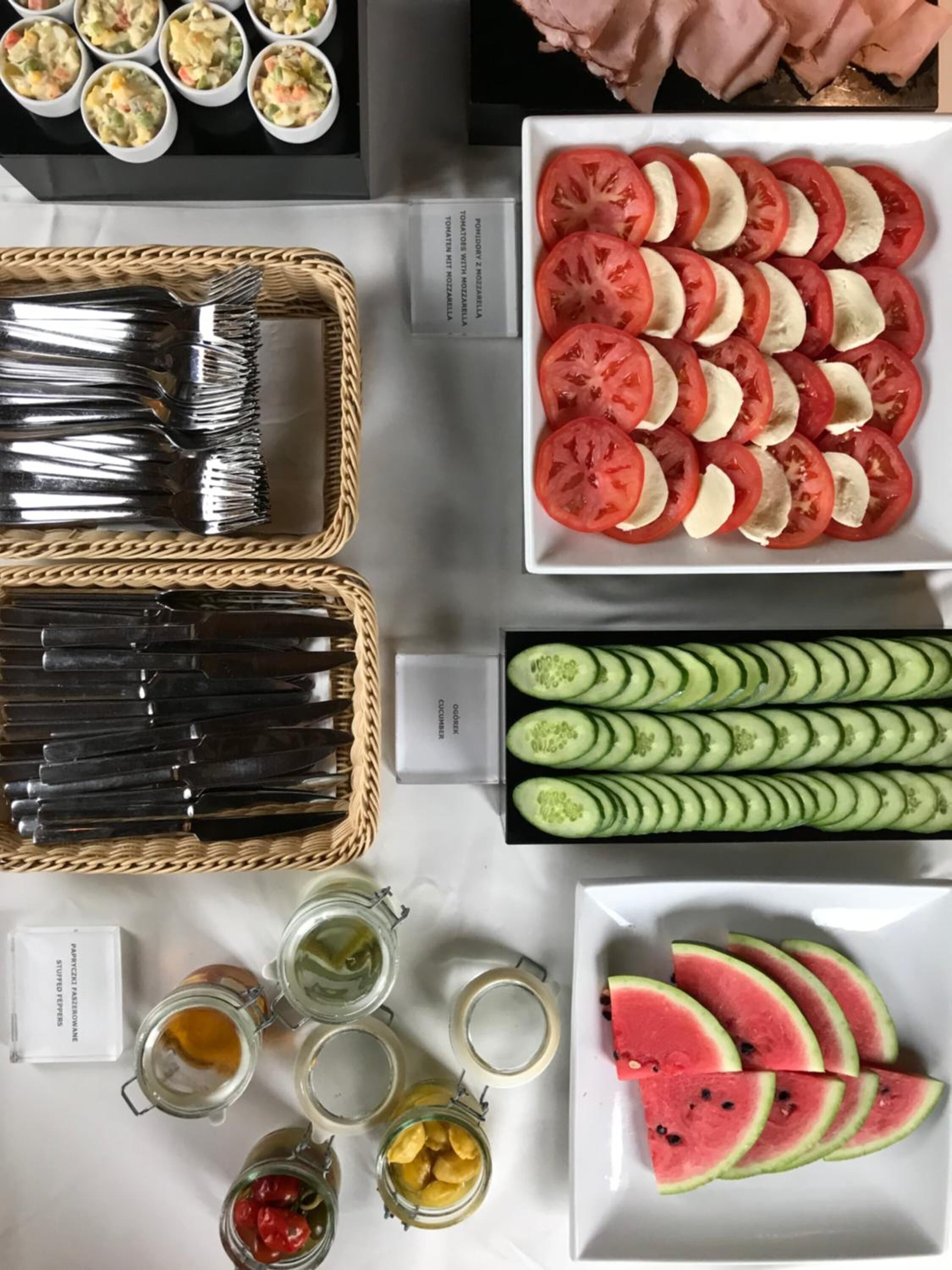A table with various food items including sliced tomatoes, cucumbers, and watermelon, along with utensils and jars.