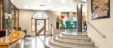 Un vestíbulo de hotel con una recepción, una escalera y un área de descanso.