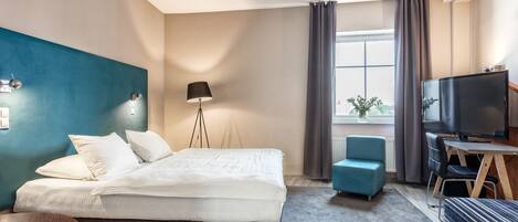 Una habitación de hotel moderna con una cama grande, un escritorio con televisor, un sillón azul y una lámpara de pie.