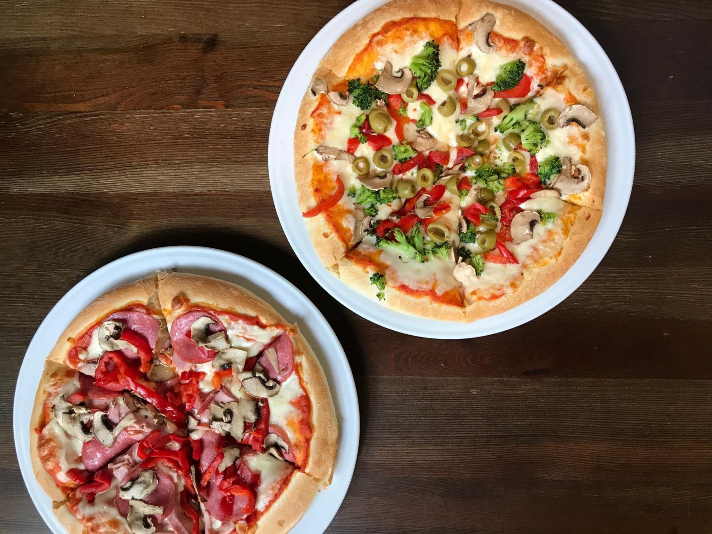 Dos pizzas sobre platos blancos en una mesa de madera.
