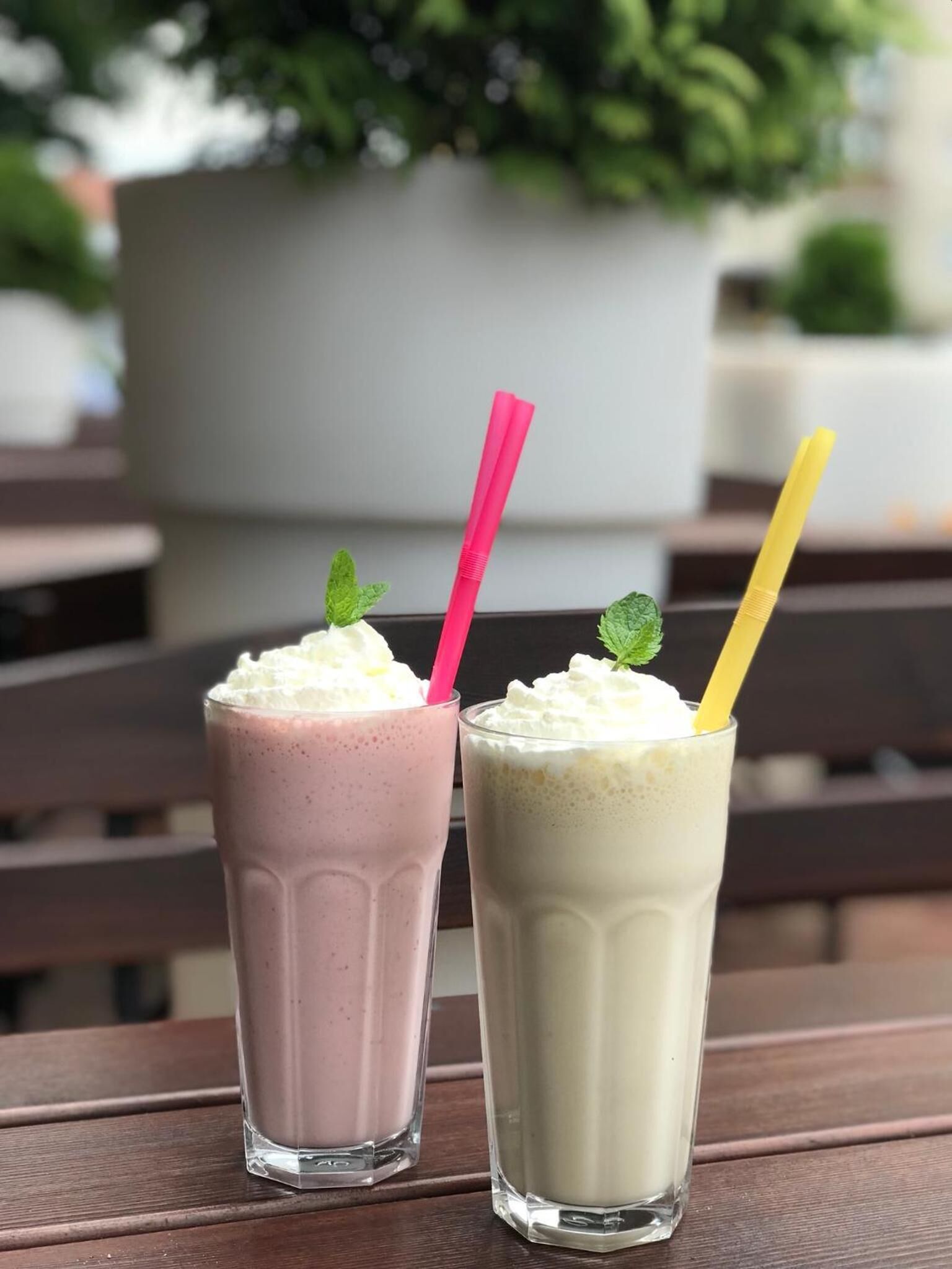 Zwei Milchshakes auf einem Holztisch vor unscharfem Hintergrund im Freien.